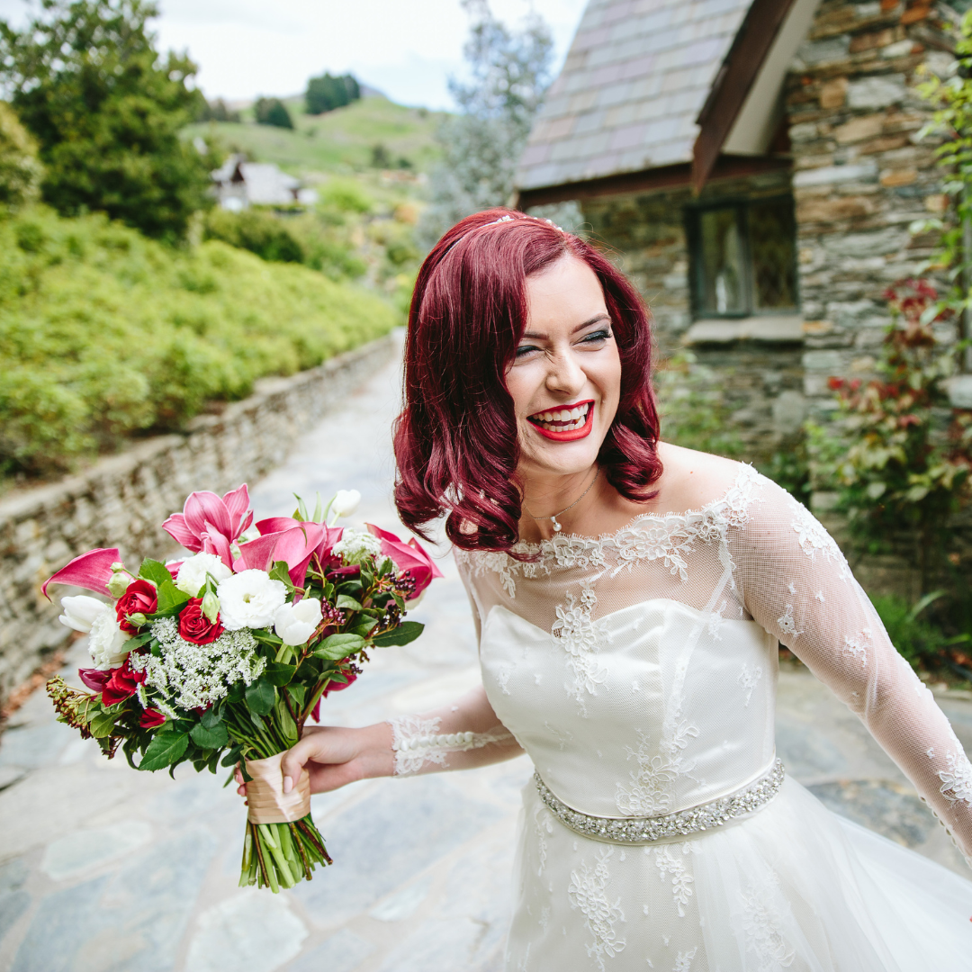 image of bride wearing redesigned wedding dress, bride is laughing and holding pink and white flower bouquet